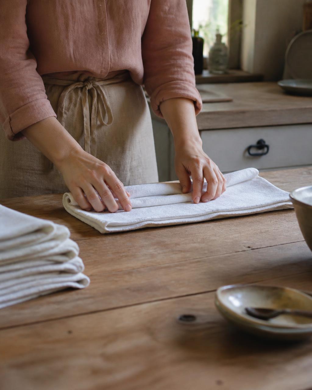 Folding fresh linens on a wooden table in a sunlit cottage kitchen